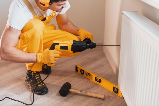 Bricoleur en uniforme jaune travaille à l'intérieur en utilisant une perceuse à percussion Conception de rénovation de maison