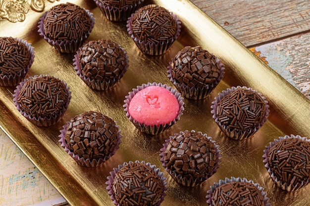 Brigadeiro aux fraises (Bicho de pe) entouré de brigadeiros (brigadiers) traditionnels. Alignés sur un plateau doré.