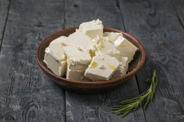 Un brin de romarin près d'un bol en argile avec des morceaux de feta. Fromage naturel au lait de brebis.