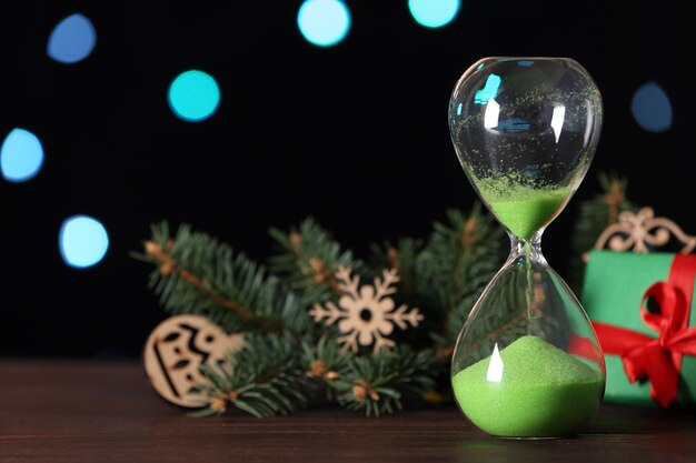 Brindille de sapin cadeau sablier et décor sur table en bois contre les lumières floues espace pour texte compte à rebours de Noël