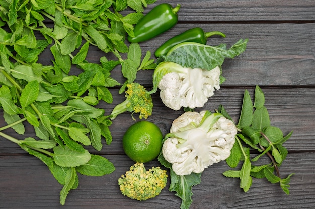 Brins de menthe, brocoli et chou-fleur. Citron vert et poivrons verts sur table. Fond de bois. Mise à plat