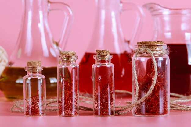 Brins de safran séchés dans une bouteille en verre et extrait d'huile sur fond rose. Le safran en cosmétologie, médecine et cuisine.