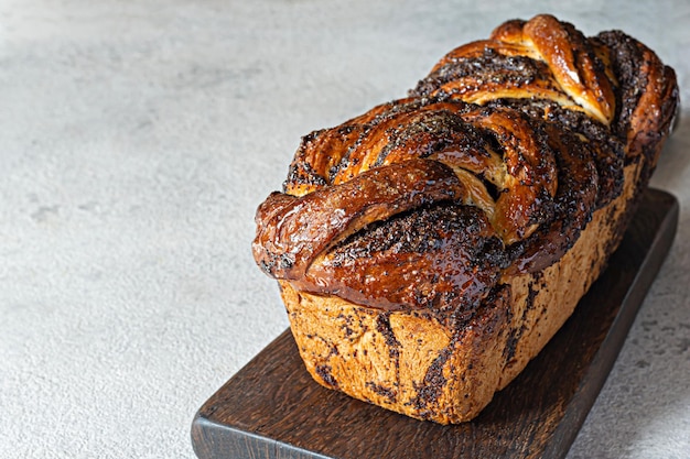 BriocheBabka fraîchement cuite avec des graines de pavot et du chocolat sur une planche de bois. Pain de dessert tressé.