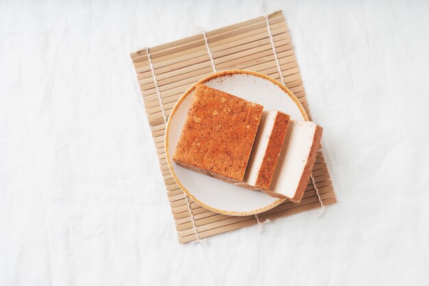 Brique de fromage tofu somoked bio servi sur une assiette blanche sur une natte de bambou. Mise à plat. Vue de dessus. Concept de collation végétalienne