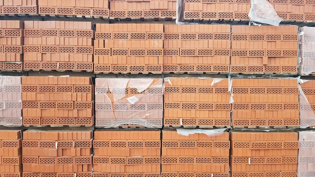 Photo briques perforées rouges avec des trous rectangulaires sur des palettes en bois dans un entrepôt en plein air prêt à la vente. de nouvelles briques sur des palettes dans une quincaillerie.