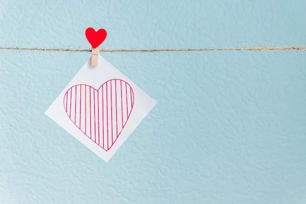 Broche de coeurs d'amour rouge Saint-Valentin suspendu à un cordon naturel sur fond bleu. coeur dessiné sur le morceau de papier.