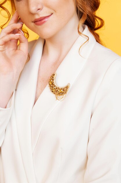 Broche de couleur dorée en forme de lune sur une veste blanche d'une fille aux cheveux roux