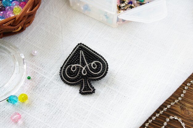 Broche perlée à la main Spades noir sur table sur fond blanc