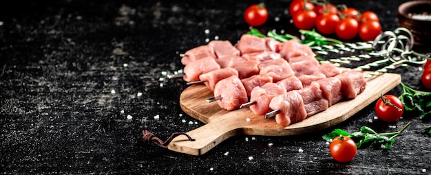 Brochette de porc crue sur une planche à découper avec tomates et persil