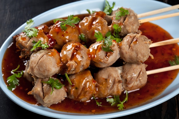 Brochettes de boulettes de viande grillées en bambou sur plaque blanche avec sauce épicée sur table en bois, boulettes de boeuf grillées au tendon street food de la Thaïlande.