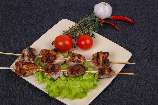 Brochettes de kebab de porc dans l'assiette avec des feuilles de salade et des tomates