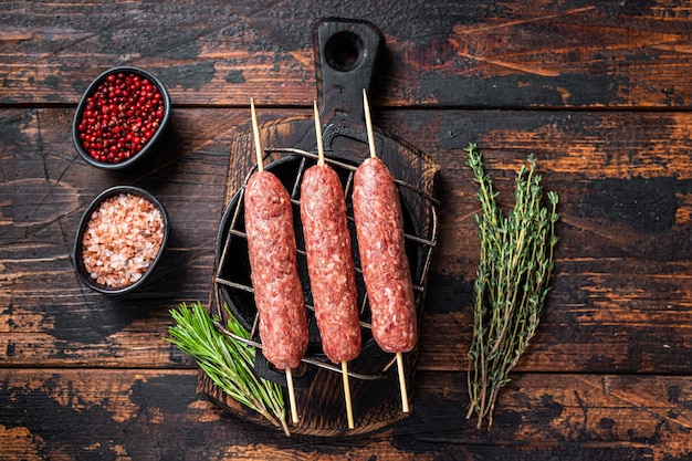 Brochettes de kofta crues ou de lula kebabs sur un grill aux herbes. Fond en bois sombre. Vue de dessus.