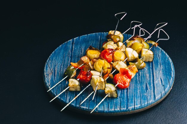 Photo brochettes de métal avec légumes grillés sur la planche de bois bleue, nourriture végétalienne