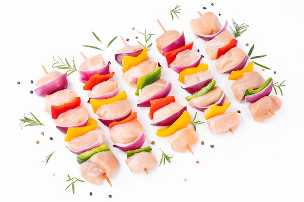 Photo des brochettes de poulet cru avec des légumes, des poivrons, des oignons sur un fond blanc, des brochettes de viande mixte non cuite.