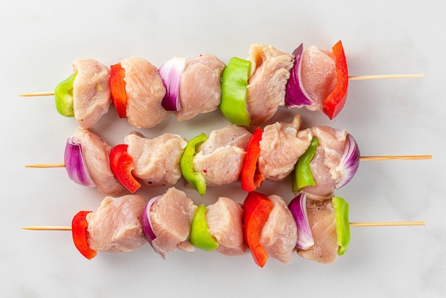 Brochettes de poulet cru avec des tranches de poivron et d'oignon pour la cuisson du shish kebab ou du barbecue sur fond blanc. vue de dessus. concept de cuisine