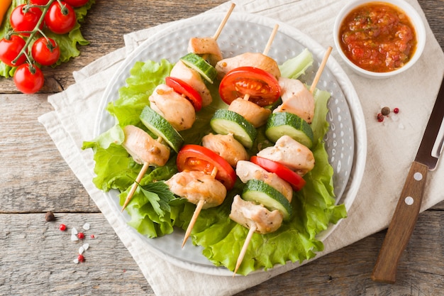 Brochettes de poulet traditionnelles sur des brochettes en bois avec des tomates, des concombres et des herbes fraîches sur une assiette