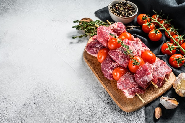 Brochettes de viande de boeuf cru sur une planche à découper.