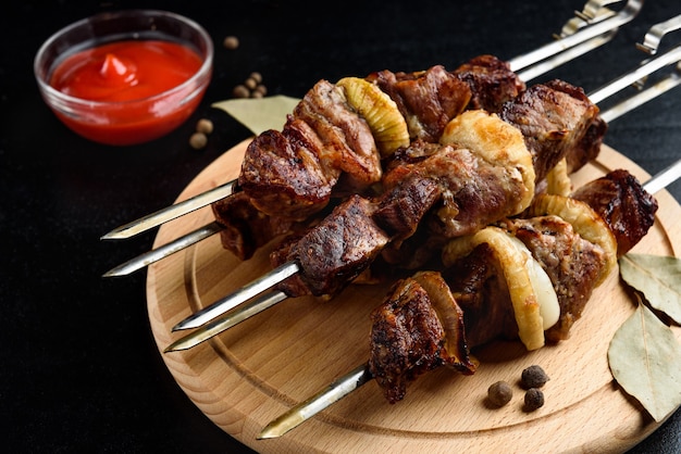 Brochettes de viande grillée, shish kebab avec ketchup et épices sur fond noir.