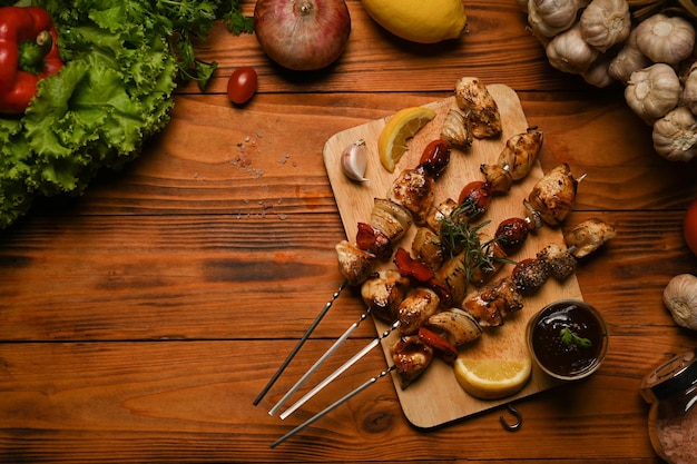 Brochettes de viande grillée avec tomates cerises, poivrons, oignons et sauce barbecue sur planche de bois Vue de dessus