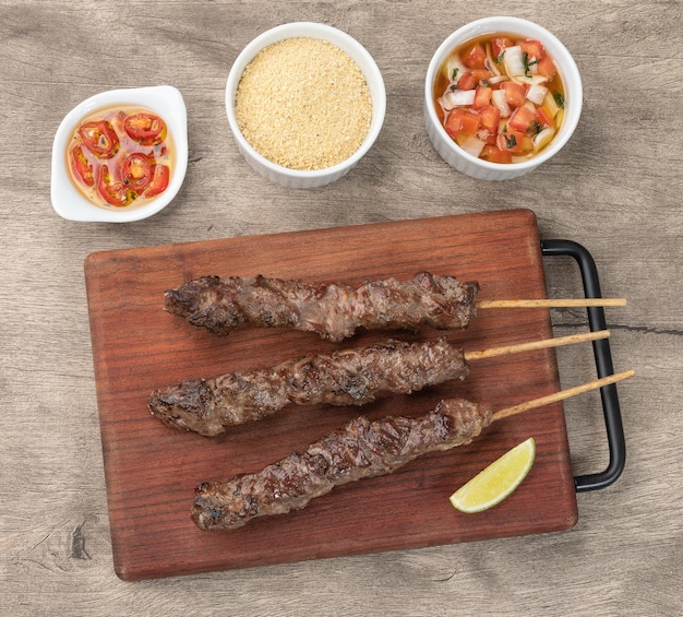 Brochettes de viande sur planche de bois avec farofa et vinaigrette