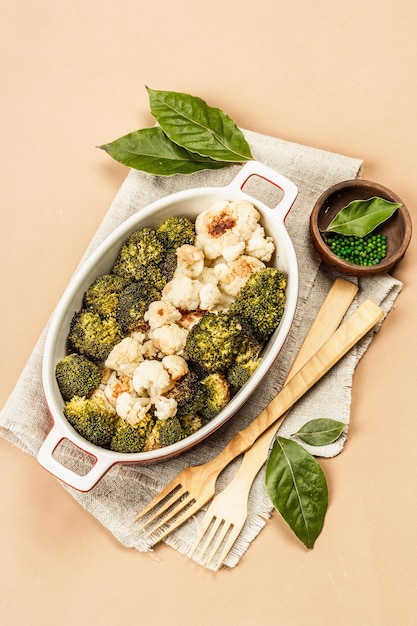 Brocoli et chou-fleur au four. Couverts en bois, feuilles de laurier fraîches, poivre vert. Concept d'alimentation saine, fond beige clair, vue de dessus