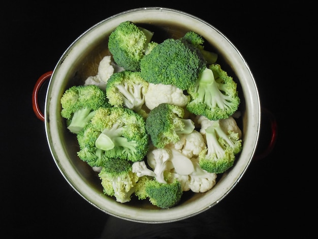 Brocoli et chou-fleur crus frais dans une casserole en métal sur un fond sombre. Fleurons de brocoli prêts pour la cuisson.