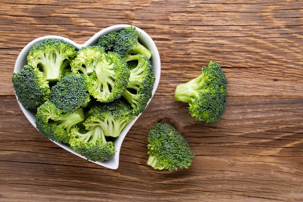 Brocoli frais dans un bol en forme de coeur sur une table en bois.