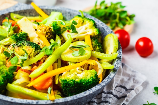 Brocoli frit, poivrons, maïs, courgettes et tomates dans une casserole sur un fond blanc.