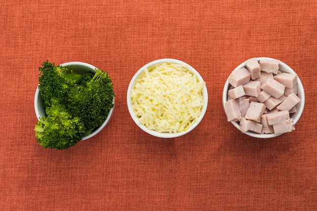 Brocoli, poitrine de dinde en dés et fromage râpé dans des pots blancs sur une table avec une nappe rouge. Mise au point sélective. Vue de dessus.