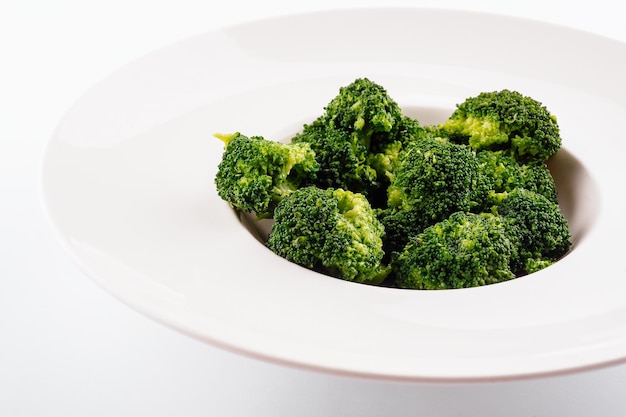 Brocoli vert frais dans une assiette de cercle blanc isolé sur blanc