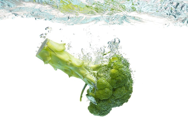 Le brocoli vert tombant dans l'eau avec des éclaboussures sur le blanc avec des bulles d'air