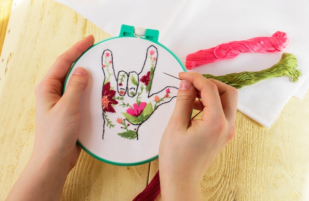 Broderie sur toile entre les mains d'une fille. Vue d'en-haut. La broderie, comme une sorte de couture, de créativité et d'art. Broderie du doigt en fleurs