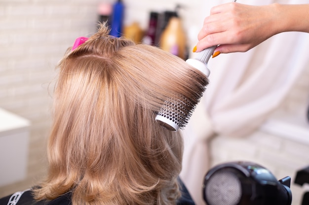 Brossage à la main du coiffeur et brushing cheveux blonds en salon de beauté