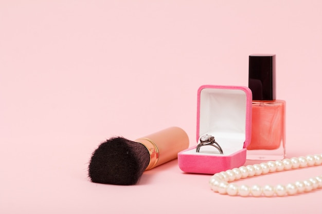 Brosse, bague dans une boîte, vernis à ongles et perles sur fond rose. Bijoux, cosmétiques et accessoires pour femmes.