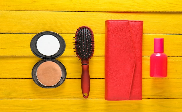 Photo brosse à cheveux, miroir, sac à main, flacon de parfum. accessoires tendance sur un fond en bois jaune. vue de dessus.