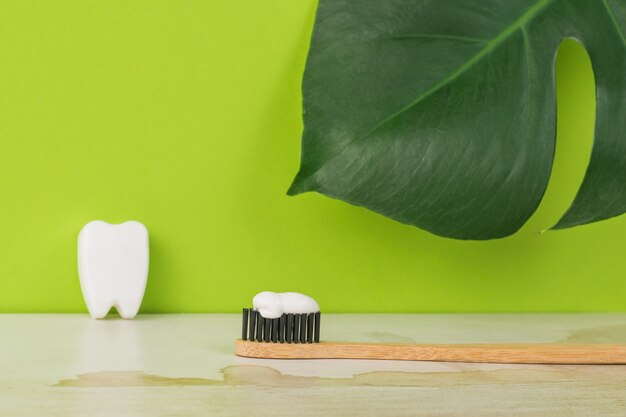 Brosse à dents en bois avec pâte sur fond de feuilles vertes.