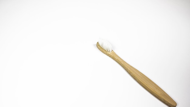 Une brosse à dents en bois avec des poils blancs est sur un fond blanc.