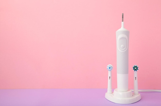 Brosse à dents électrique moderne avec têtes de rechange et chargeur sur fond rose