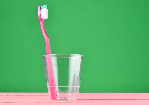 Brosse à dents rose dans une tasse transparente sur fond pastel vert menthe