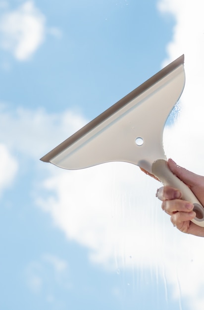 Photo brosse à fenêtre à la main lave une fenêtre avec un ciel bleu