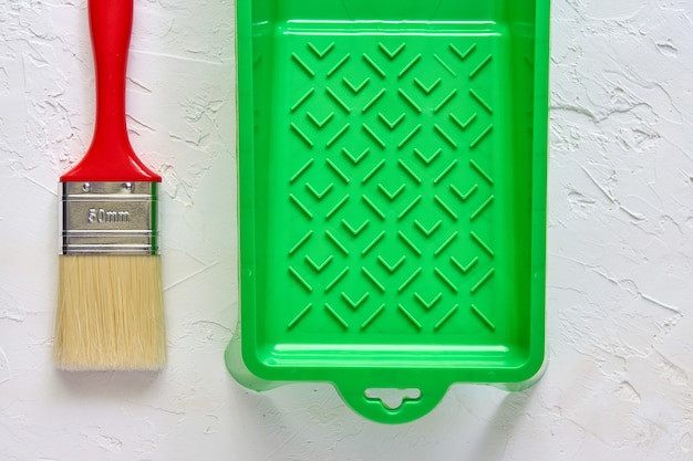 Brosse avec manche rouge et bac à peinture verte sur béton blanc. outils et accessoires pour la rénovation domiciliaire. Vue de dessus