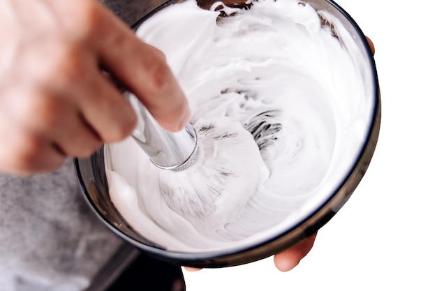 une brosse métallique fouette la mousse de savon dans une tasse Préparation pour l'élimination des chaumes de barbe