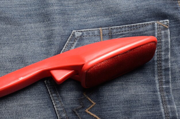 Une brosse en plastique rouge pour nettoyer les vêtements se trouve sur un jean noir.