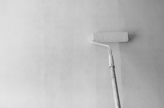 Brosse à rouleau à long manche appliquant une peinture blanche d'apprêt sur fond de mur de ciment