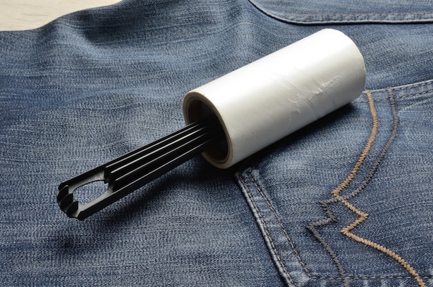 Une brosse à vêtements collante enroulée repose sur un jean foncé.