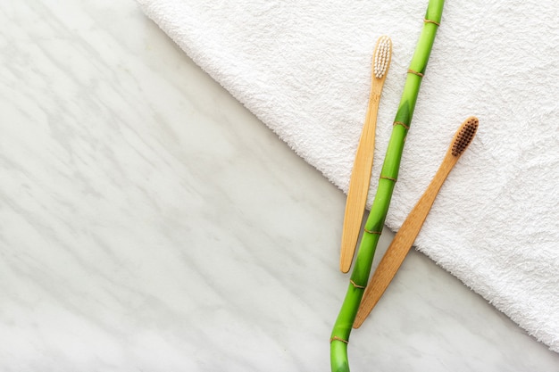 Brosses à dents en bambou, plante en bambou sur une serviette blanche, fond de marbre. Mise à plat.