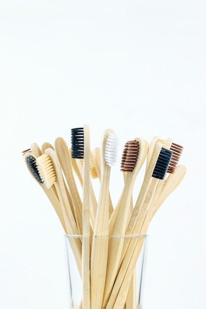 Brosses à dents en bambou respectueuses de l'environnement dans un verre transparent sur un gros plan de mur blanc. Concept zéro déchet, consommation consciente. Verticale