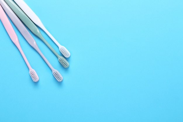 Brosses à dents roses, vertes, blanches et grises sur mur bleu.