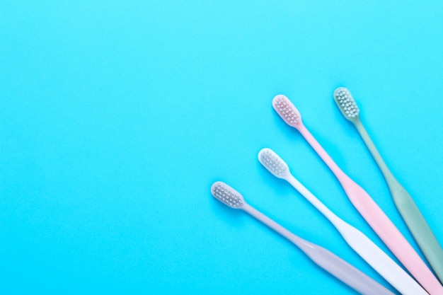 Brosses à dents roses, vertes, blanches et grises sur mur bleu.