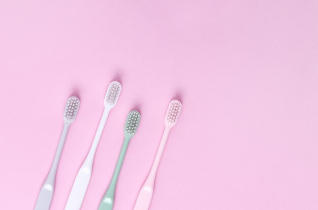 Brosses à dents roses, vertes, blanches et grises sur mur rose.